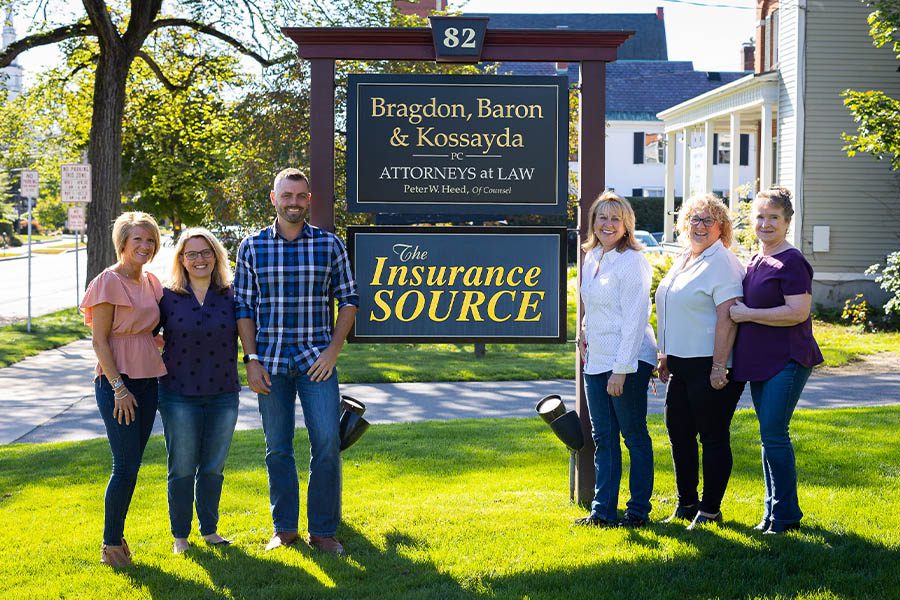 About Our Agency - Group Portrait of the Insurance Source Team Standing in Front of Their Business Office Sign Outdoors on a Sunny Day